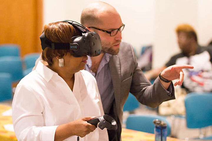 A man speaks to a woman wearing a virtual reality headset.